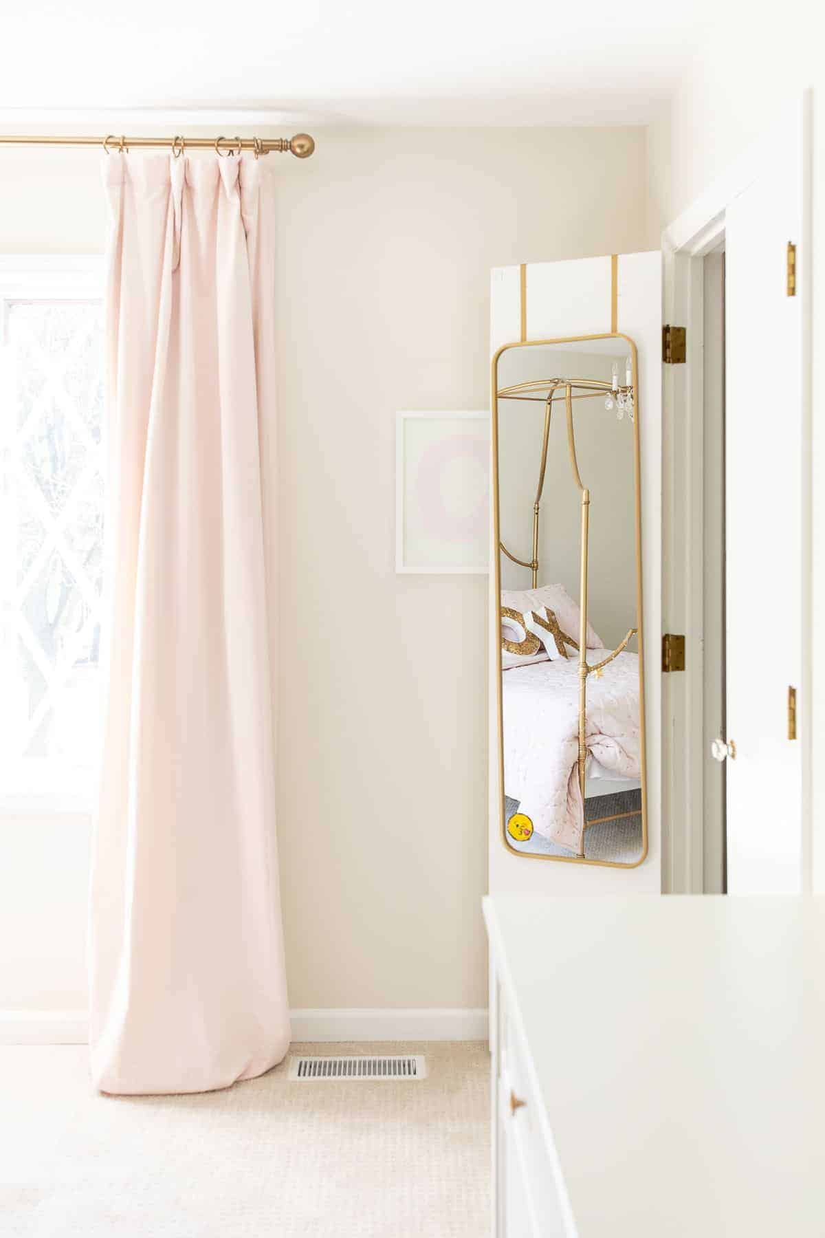 A tween girl bedroom with pink curtains and a gold mirror on the inside of closet door.