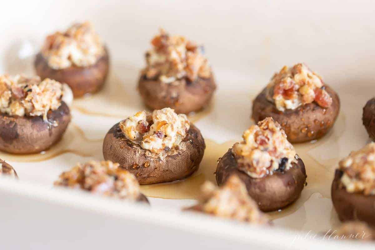 A white platter full of stuffed mushrooms on a marble surface.