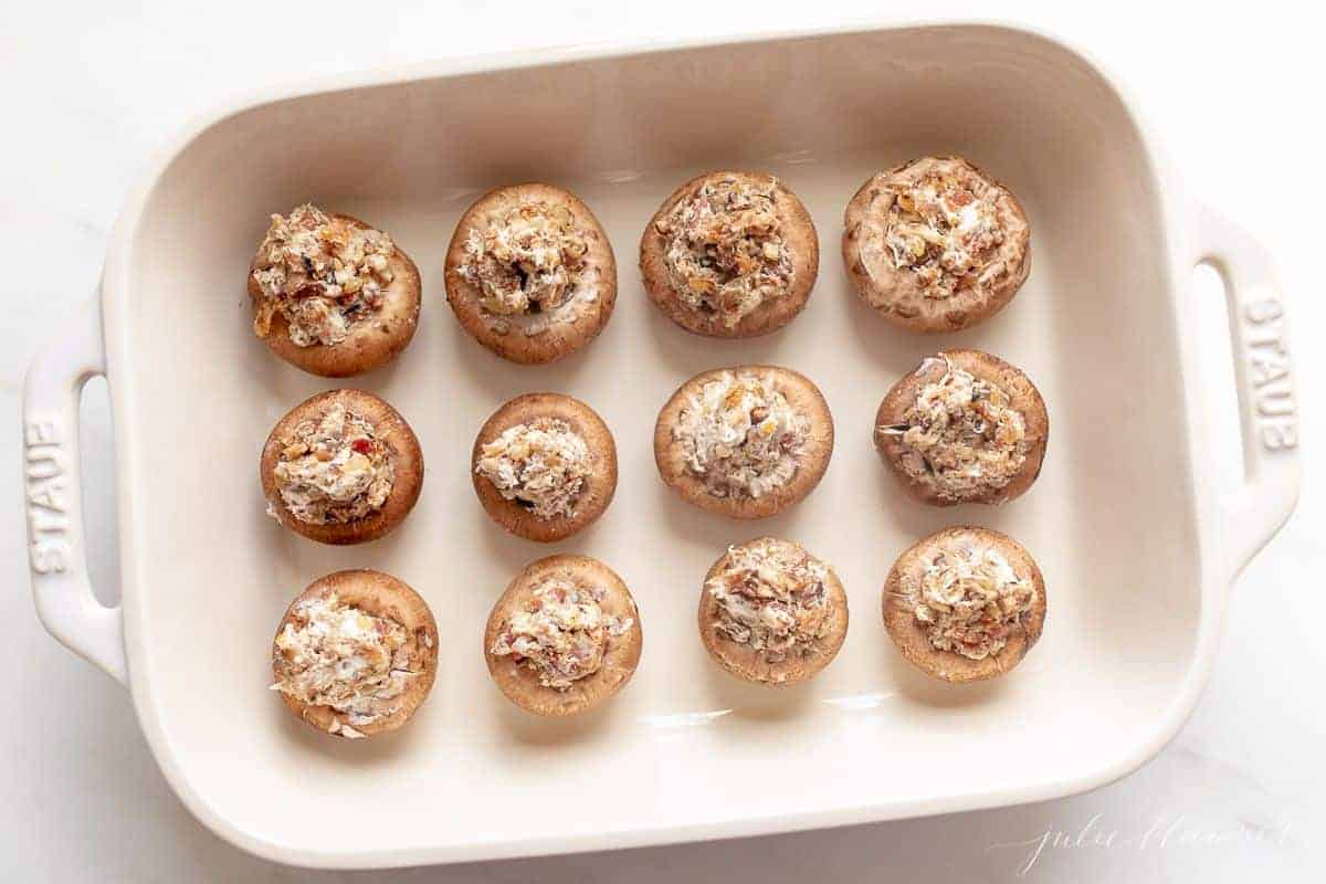 A white platter full of stuffed mushrooms on a marble surface.