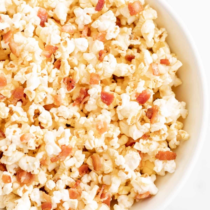 A white bowl filled with popcorn with bacon pieces