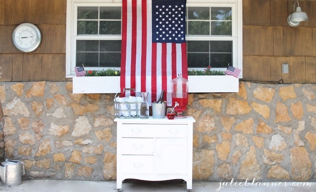 A mini Fourth of July themed bar, with red punch, white and navy striped towels, and an American Flag hanging above it. 