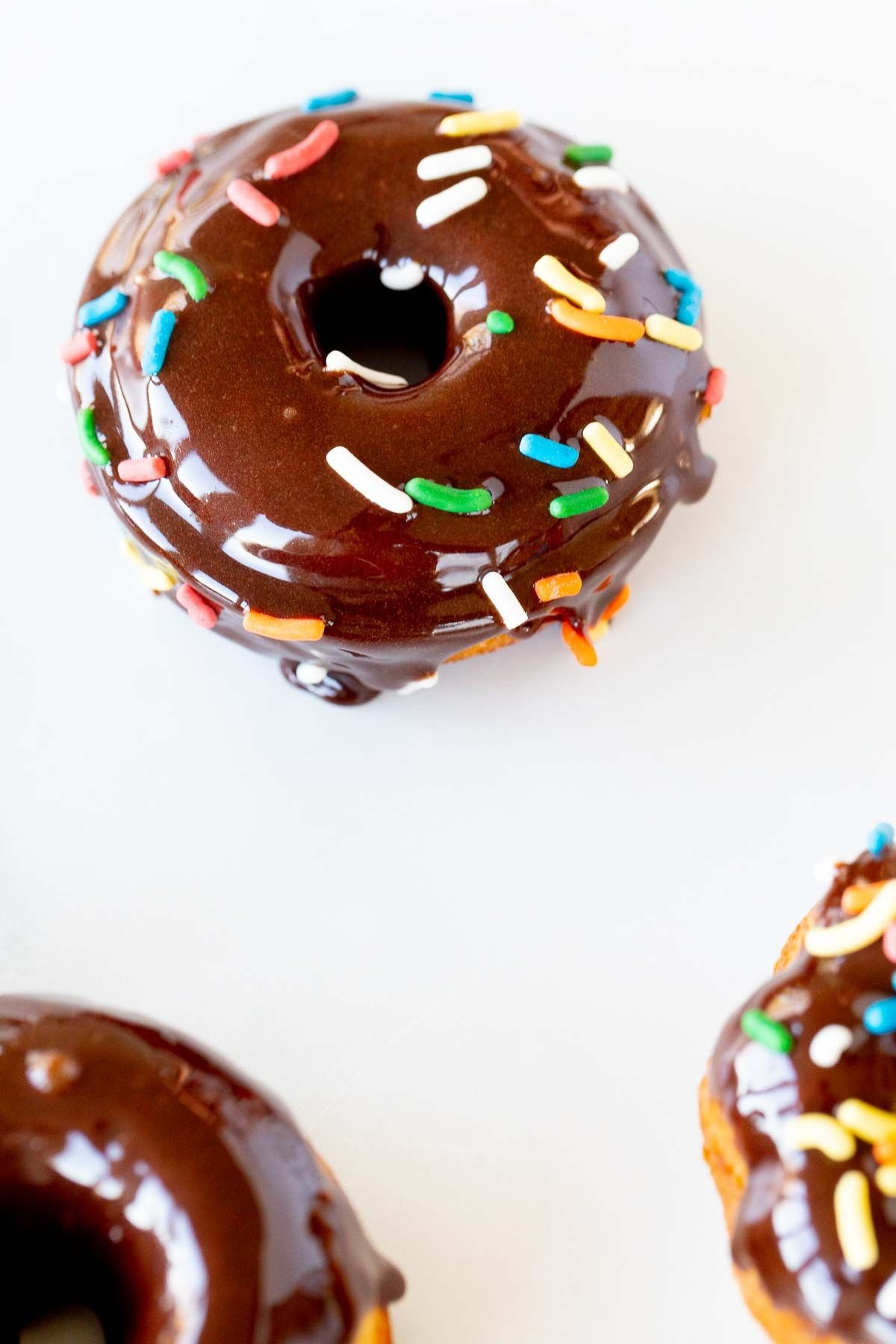 Baked donuts topped with chocolate frosting and sprinkles, on a marble countertop.