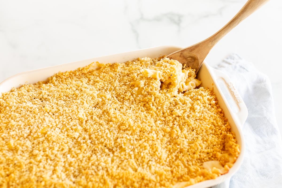 Baked macaroni and cheese in a white dish with a wooden spoon.