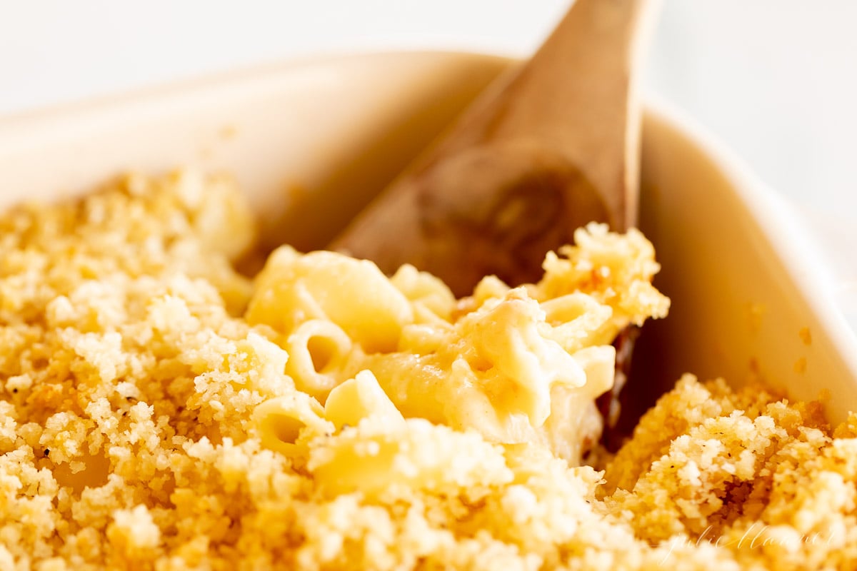 Macaroni and cheese in a white dish, served with a wooden spoon.