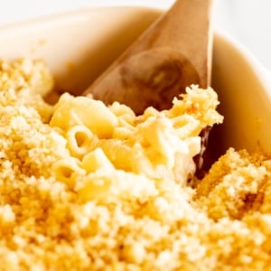 A deliciously baked macaroni and cheese dish, served in a white ceramic dish with a wooden spoon.