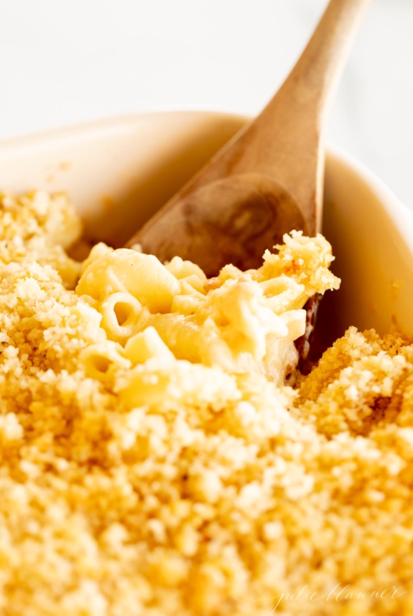 A deliciously baked macaroni and cheese dish, served in a white ceramic dish with a wooden spoon.