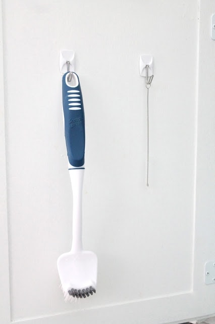Cleaning tools hanging from 3m hooks inside the door of an under sink kitchen cabinet storage project.