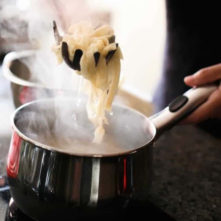 removing homemade pasta from pot of boiling water with pasta spoon