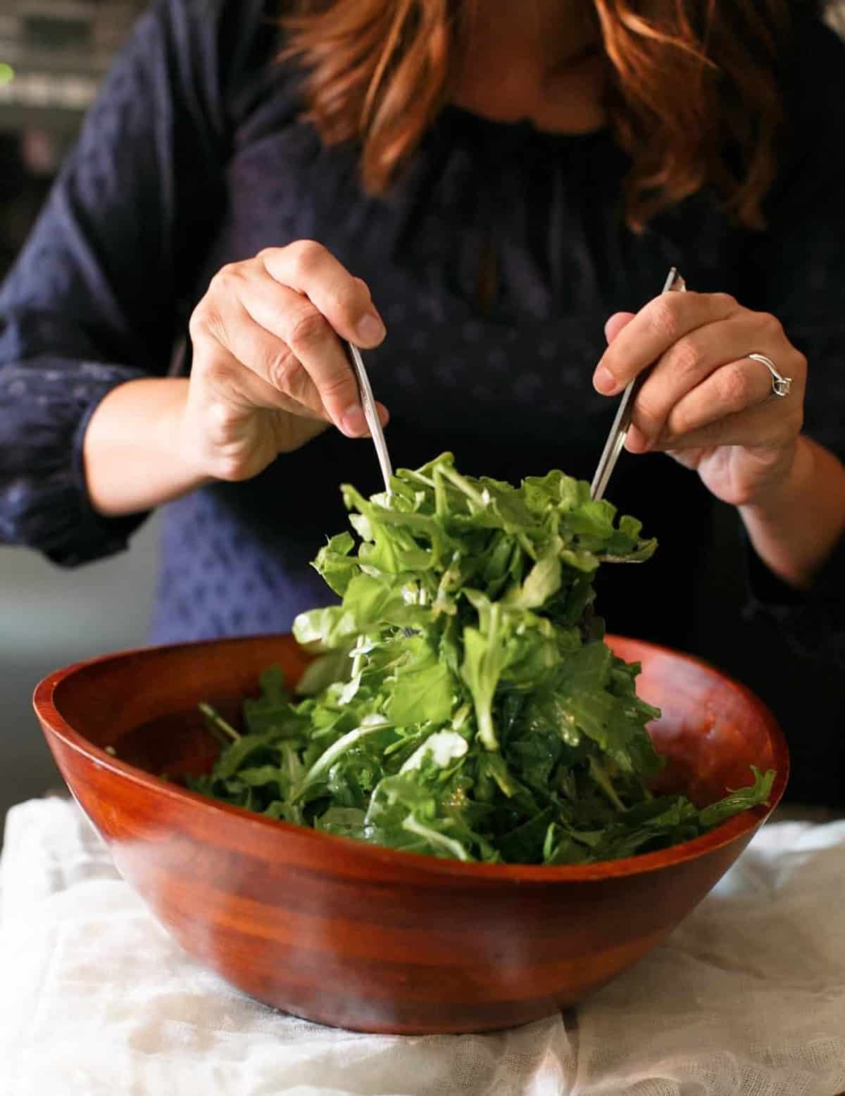 two hands tossing salad in a large brown bowl