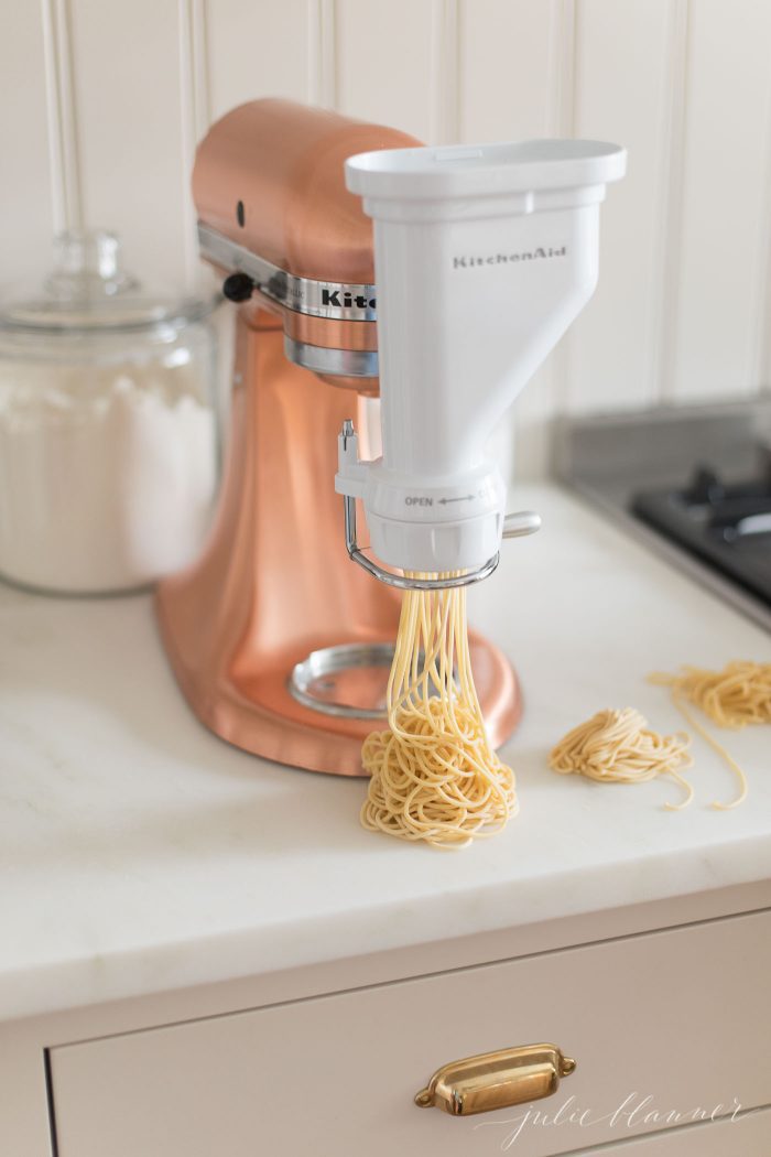 Pasta being made with a pasta maker. Noodles sit on the countertop. 