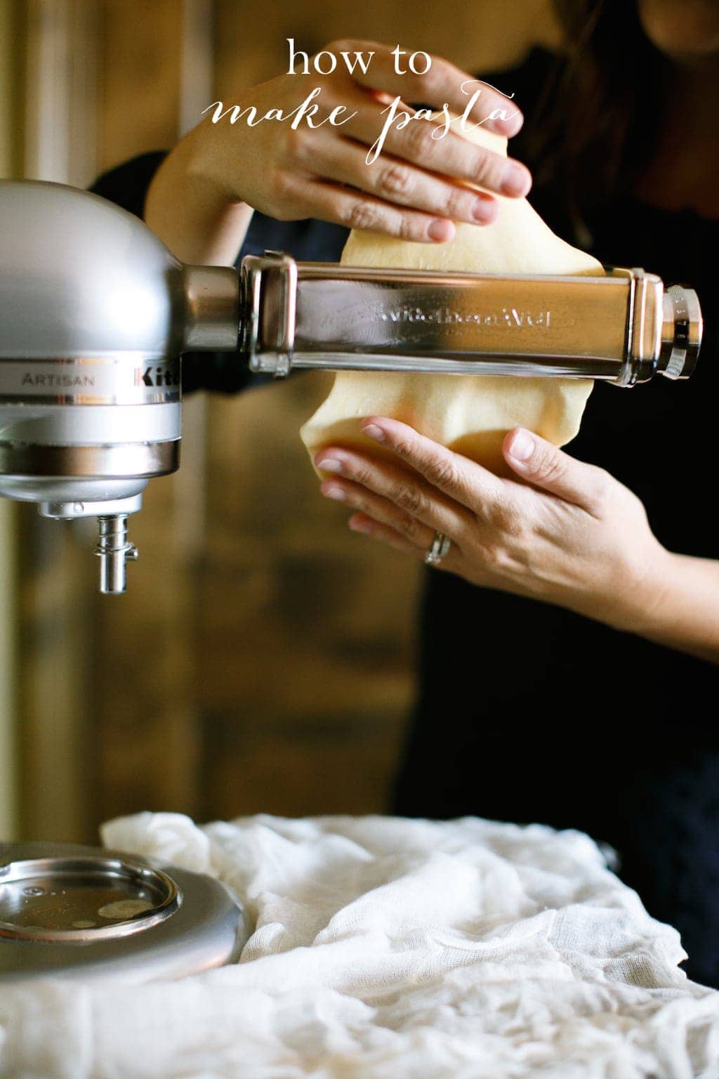 Hands pull pasta through a Kitchenaid pasta maker attachment.