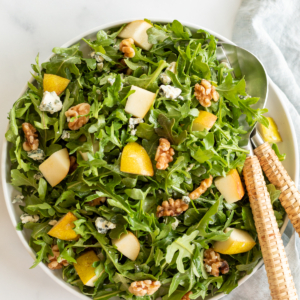 A white bowl full of pear salad, with arugula, walnuts and gorgonzola.