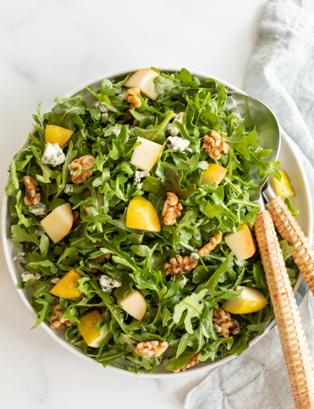 A white bowl full of pear salad, with arugula, walnuts and gorgonzola.