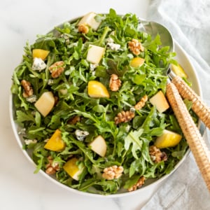 A white bowl full of pear salad, with arugula, walnuts and gorgonzola.