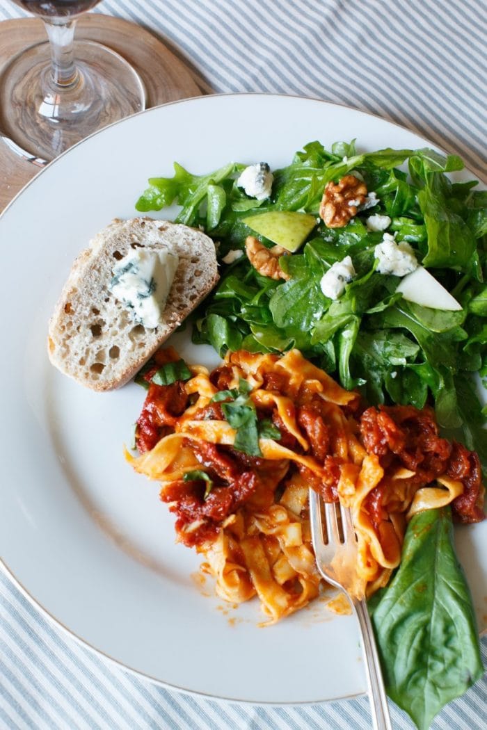 sun dried tomato pasta with salad and bread on white plate