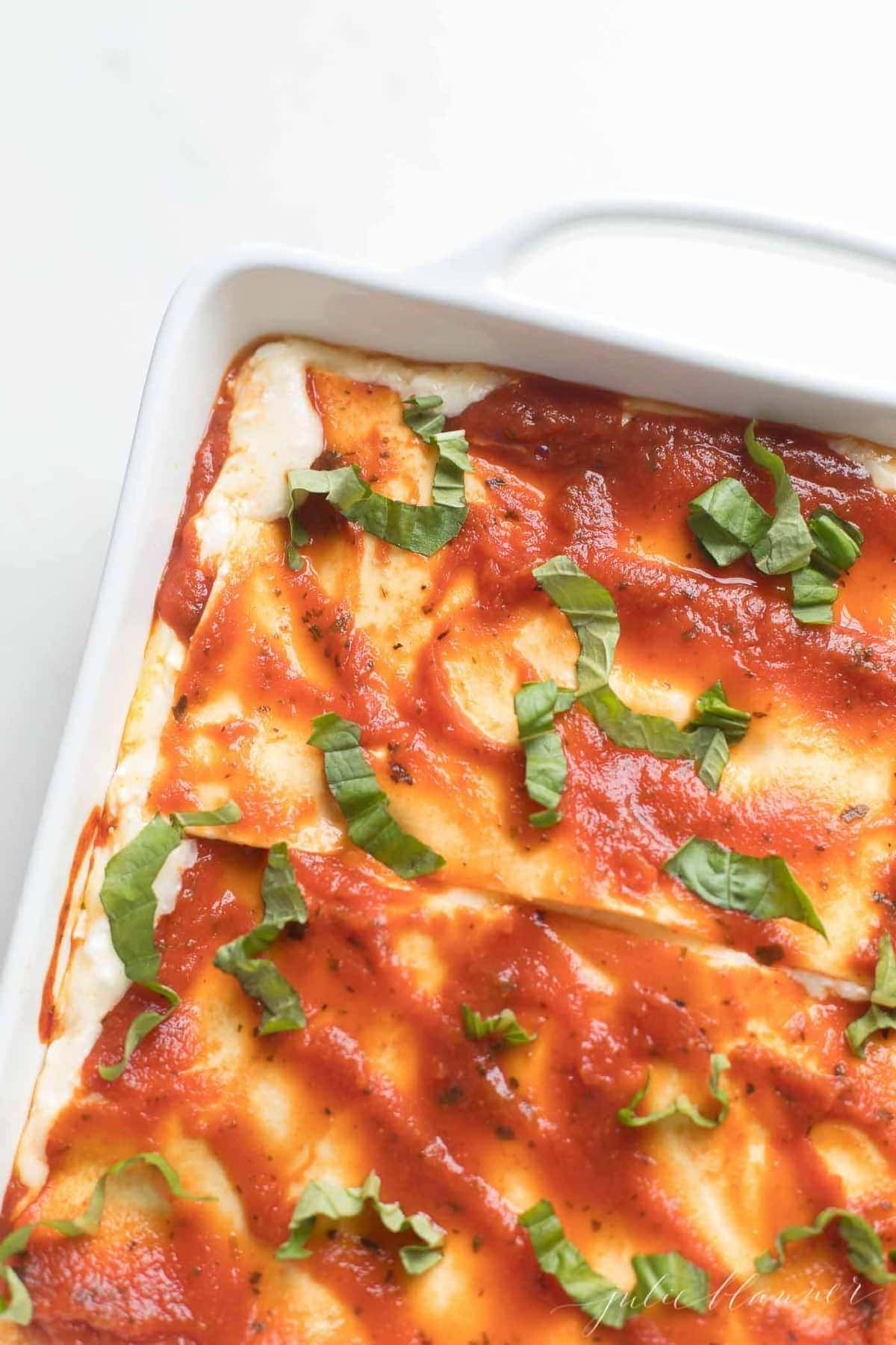 overhead of homemade lasagna with cottage cheese in white dish garnished with basil