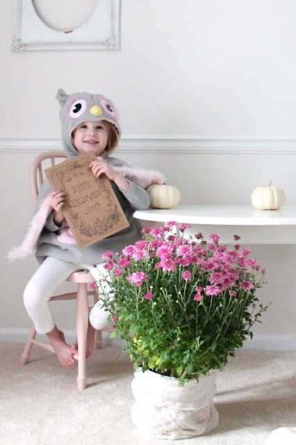 A girl dressed up holding a printable with flowers and pumpkins next to her.