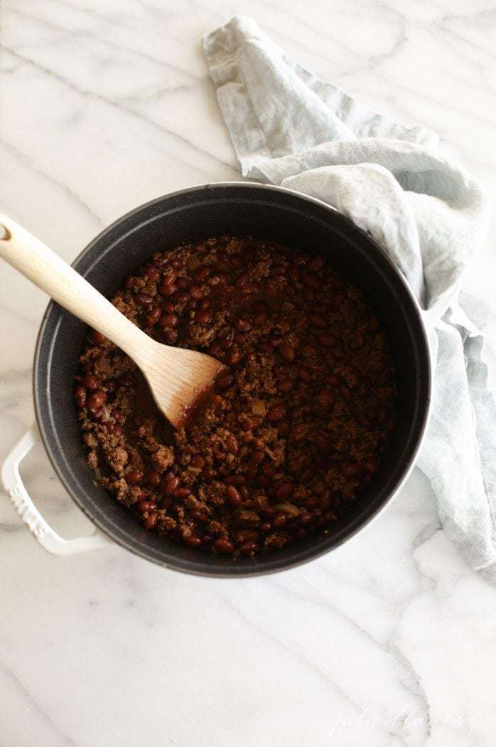 chili in white cast iron pot with wooden spoon