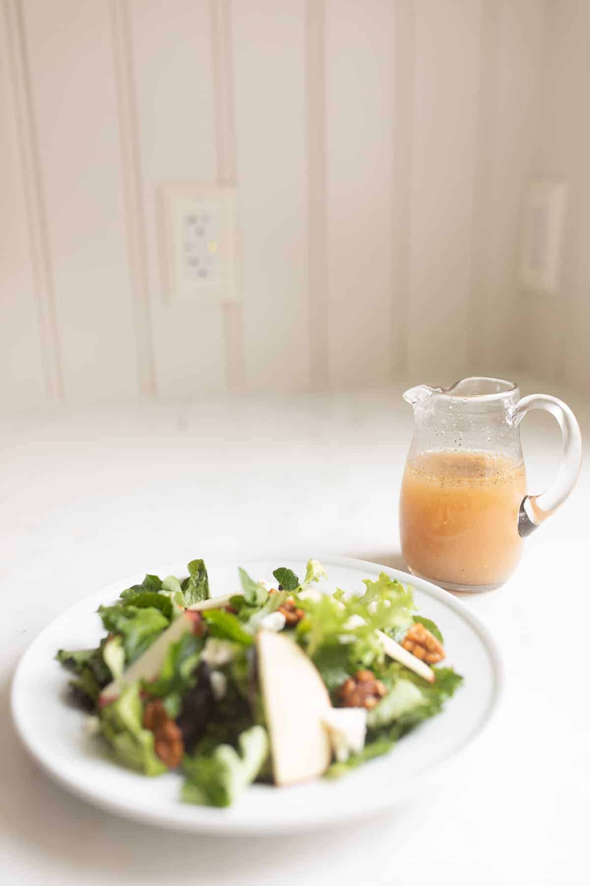 salad with apples next to apple cider vinaigrette in small clear glass pitcher