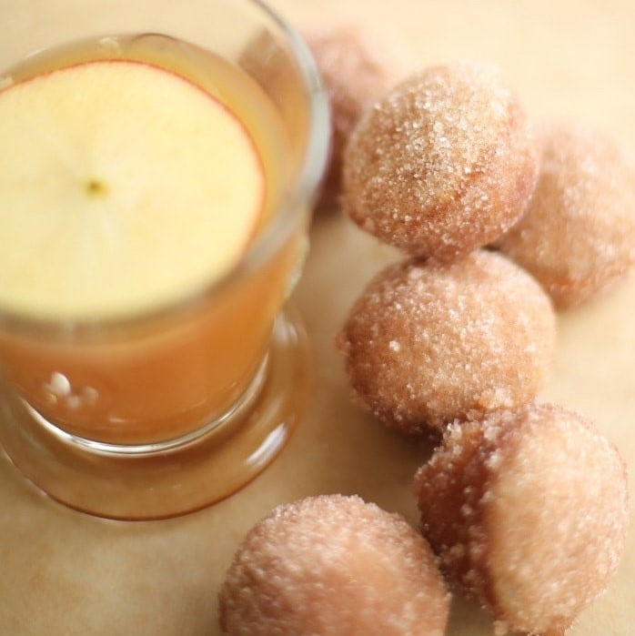 Apple cider donut holes with a small glass of apple cider next to them.