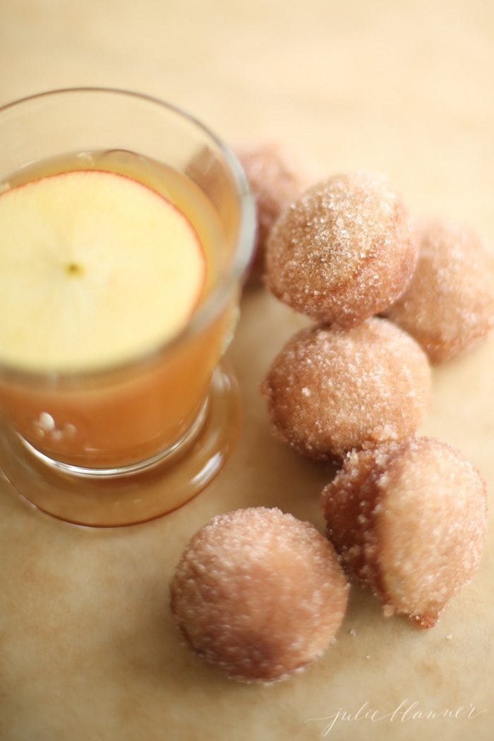 Apple cider donuts with a glass of apple cider to the side. 