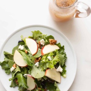 Apple cider vinegar dressing in a glass pitcher next to a plate of fresh salad.