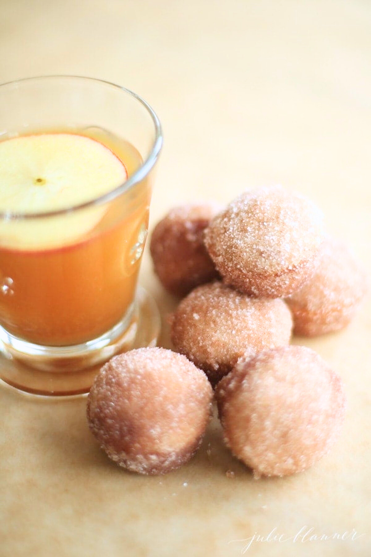 A small glass of apple cider surrounded by apple cinnamon donut holes.