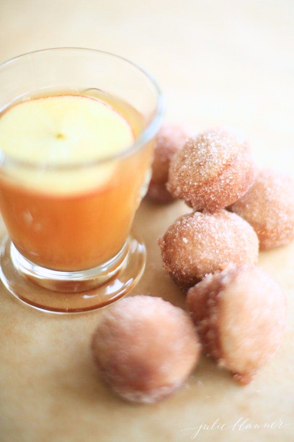 A small glass of apple cider surrounded by apple cinnamon donut holes.