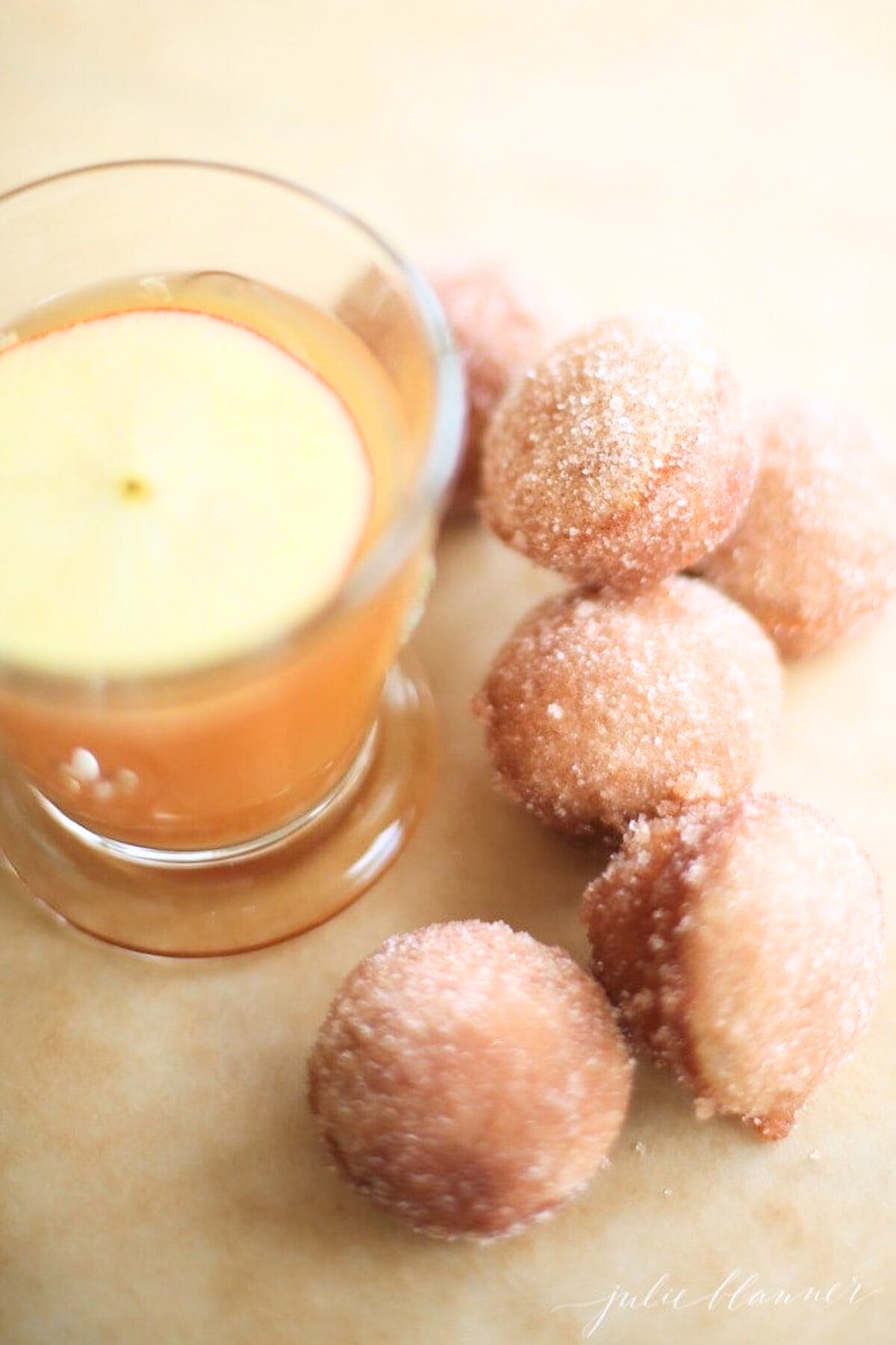 A small glass of apple cider surrounded by apple cinnamon donut holes. 