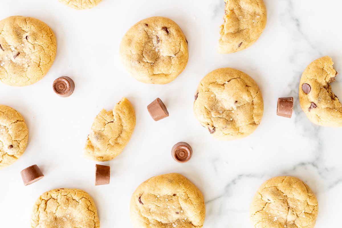 Salted caramel chocolate chip cookies on a marble countertop, surrounded by chocolate rolos.