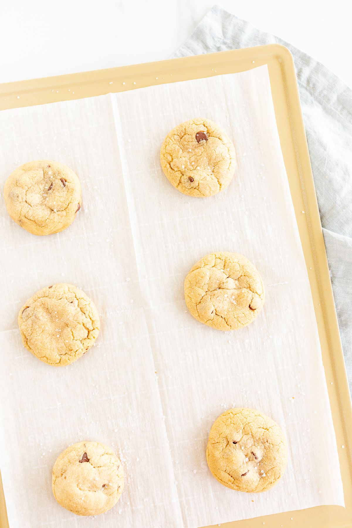 Salted caramel chocolate chip cookies on a parchment lined baking sheet.