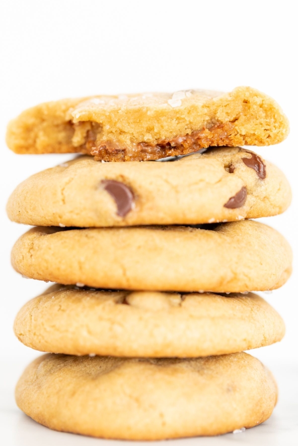 A salted caramel chocolate chip cookie, broken into two pieces., on a stack of cookies.
