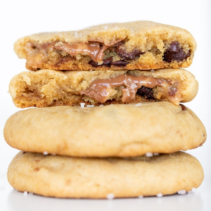 A salted caramel chocolate chip cookie, broken into two pieces., on a stack of cookies.