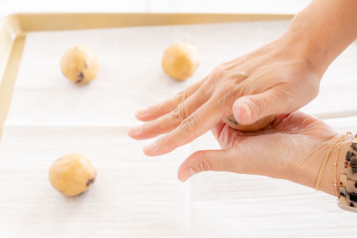 Hands rolling a ball of cookie dough to place on a baking sheet.