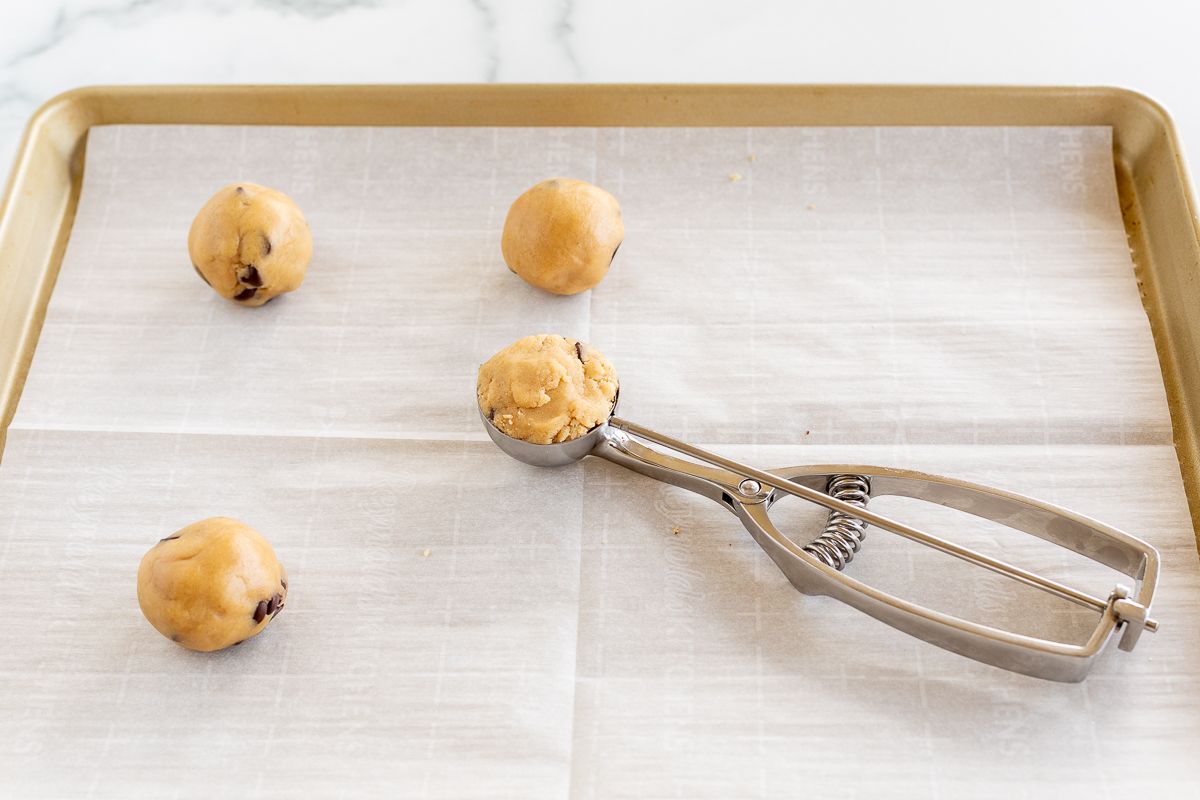 A cookie dough scoop adding cookie dough to a parchment lined baking sheet.