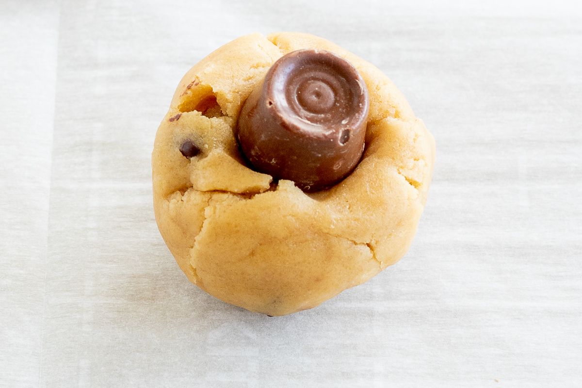 A rolo candy resting on top of a ball of cookie dough.