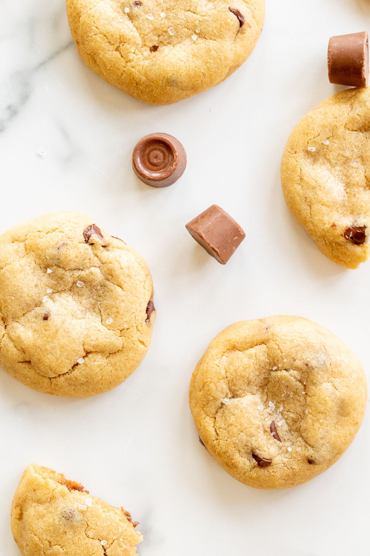 Salted caramel chocolate chip cookies on a marble countertop, surrounded by chocolate rolos.