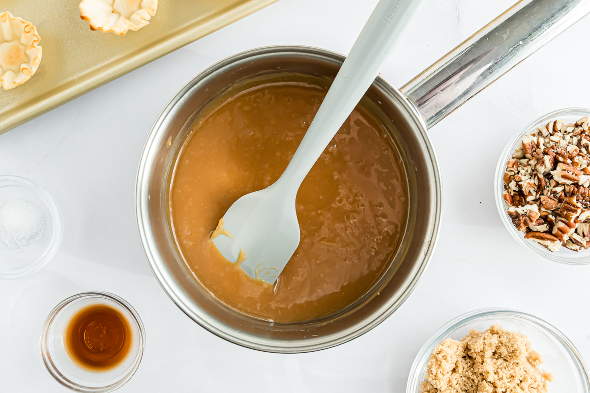 A pot of caramel sauce with a spoon and other ingredients, perfect for pecan pie bites or mini pecan pies.