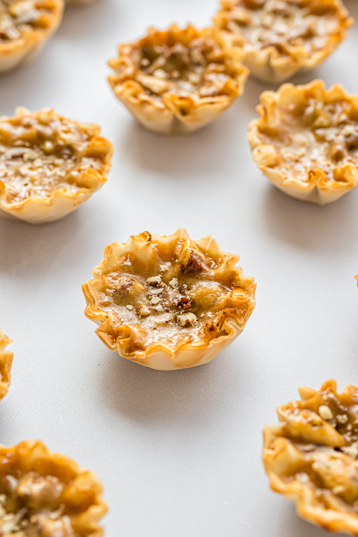 A group of Mini Pecan Pie tarts on a white surface.