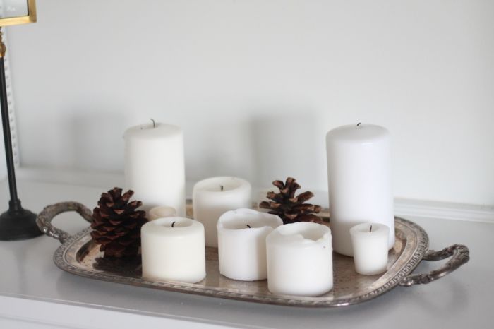 Winter decor of white pillar candles and pine cones on a silver tray.