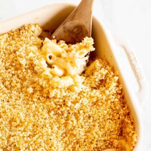 A white baking dish full of bacon mac and cheese, wooden spoon scooping at the edge.