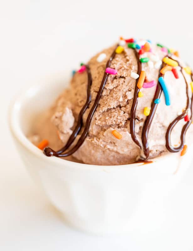 chocolate snow ice cream topped with sprinkles and fudge in white bowl