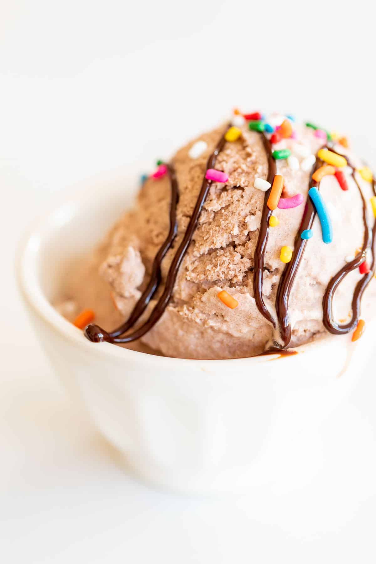 chocolate snow ice cream topped with sprinkles and fudge in white bowl