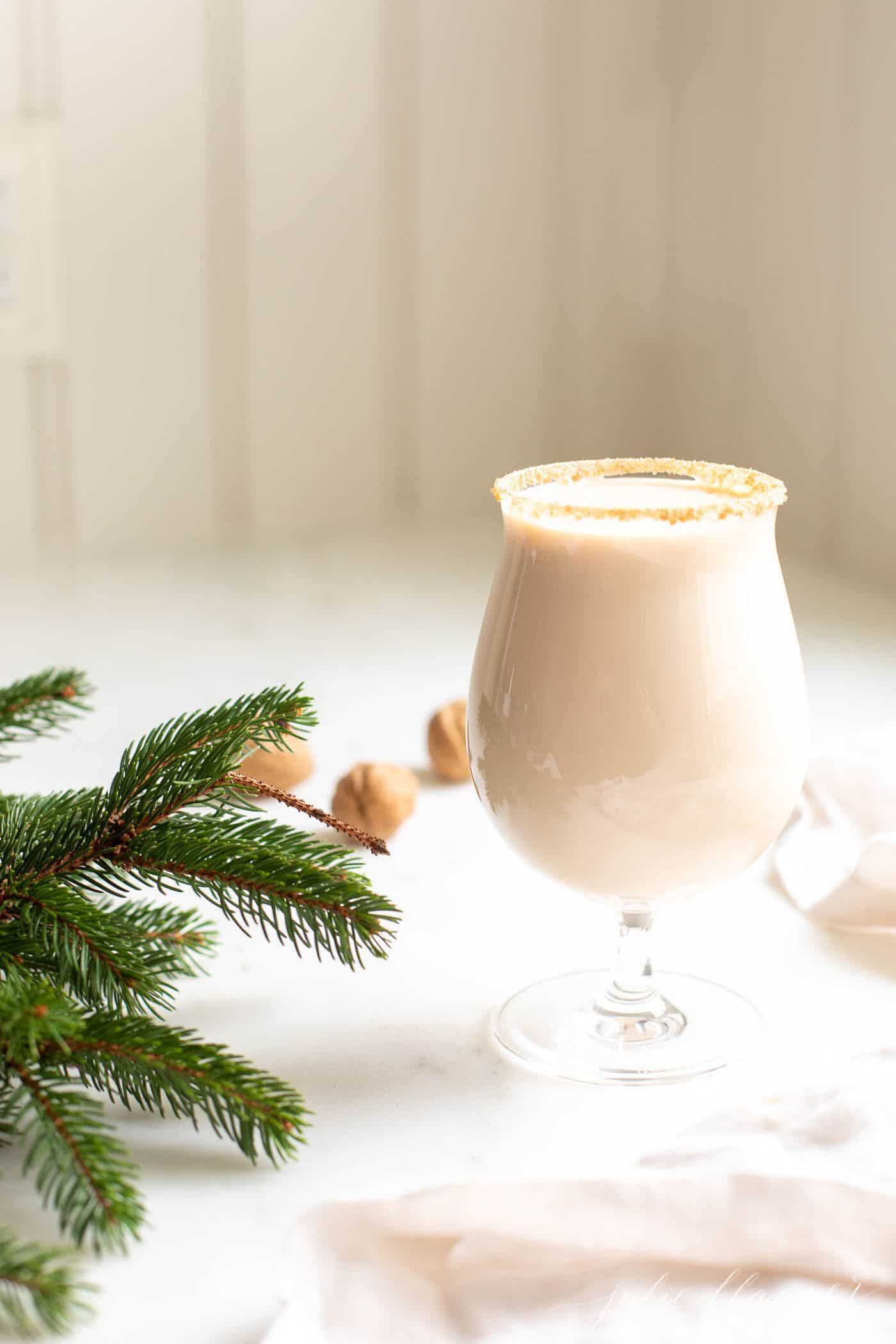 A clear glass filled with an oatmeal cookie Christmas cocktail, greenery and hazelnuts in the background.