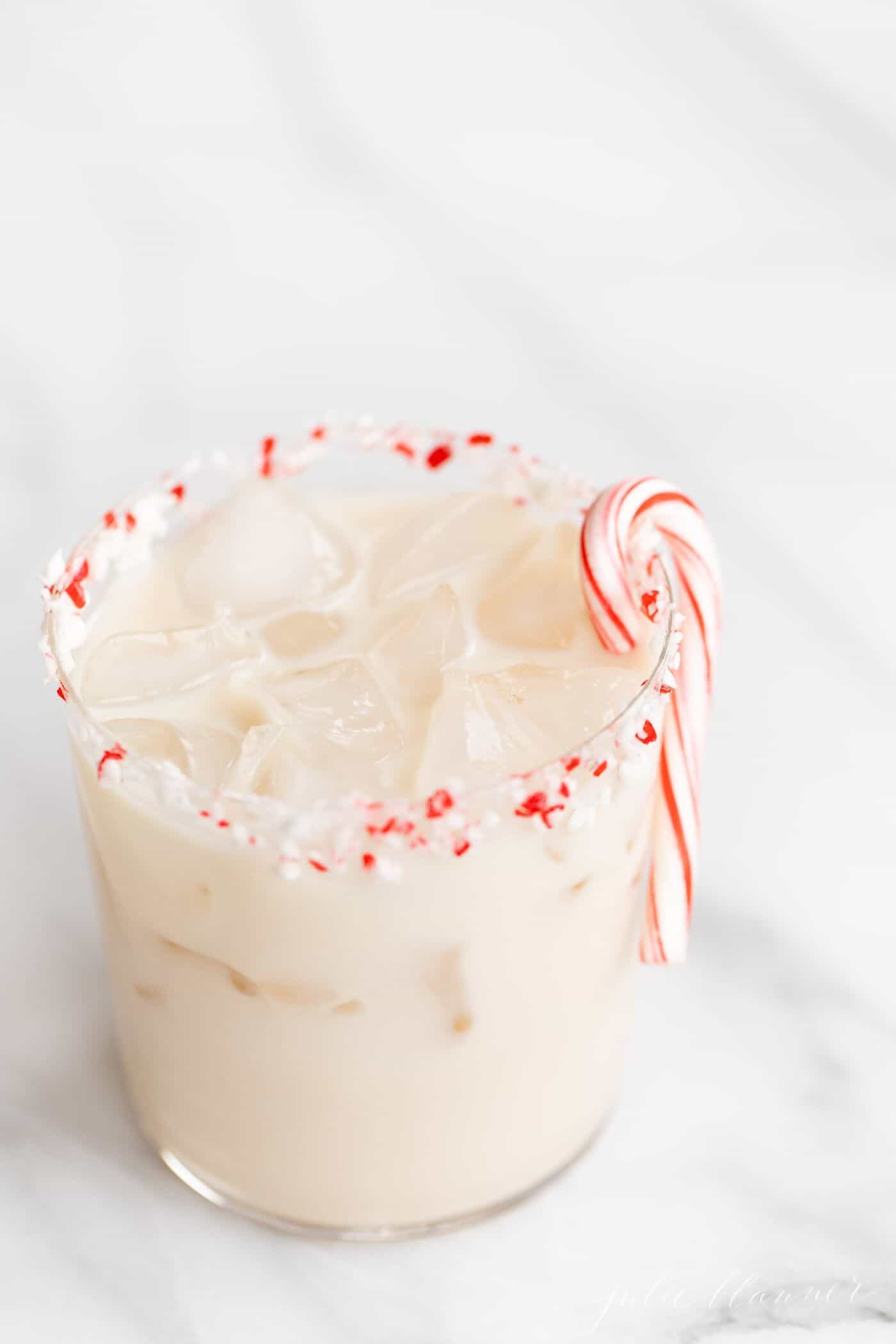A clear glass full of a peppermint Christmas cocktail on a marble surface.