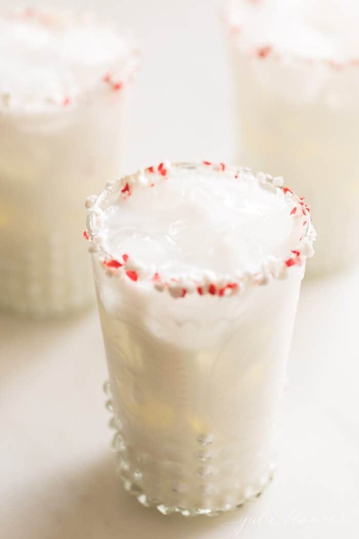 A creamy white cocktail in a clear glass, rimmed with crushed peppermint.