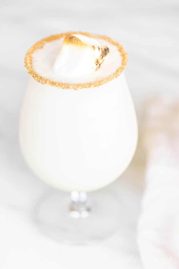 A clear stemmed glass filled with a white Christmas cocktail, topped with a marshmallow and a sugared rim.