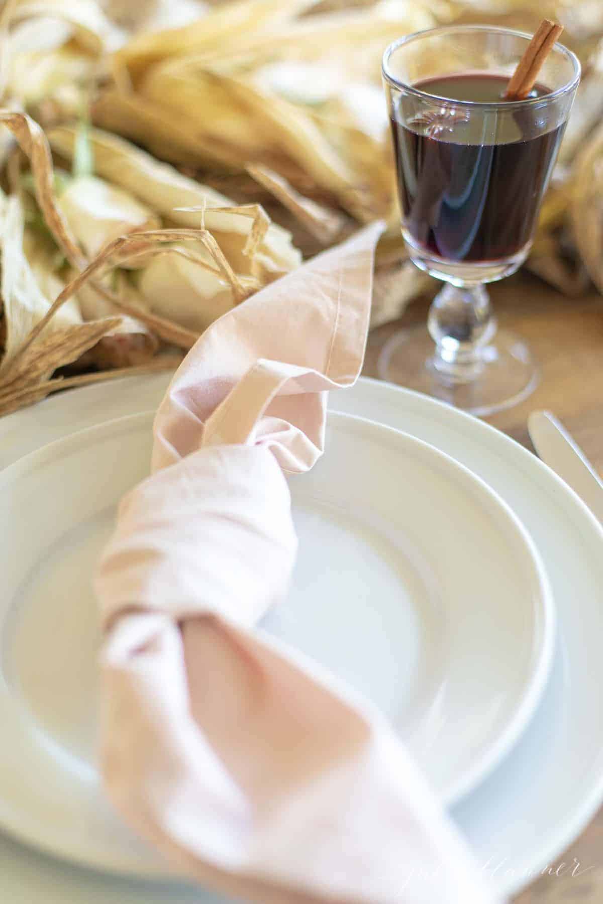 A Thanksgiving cocktail in a clear glass next to white plates and a pink napkin.
