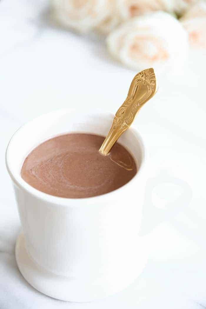 A white mug with a Thanksgiving drink of hot chocolate, gold spoon inside.