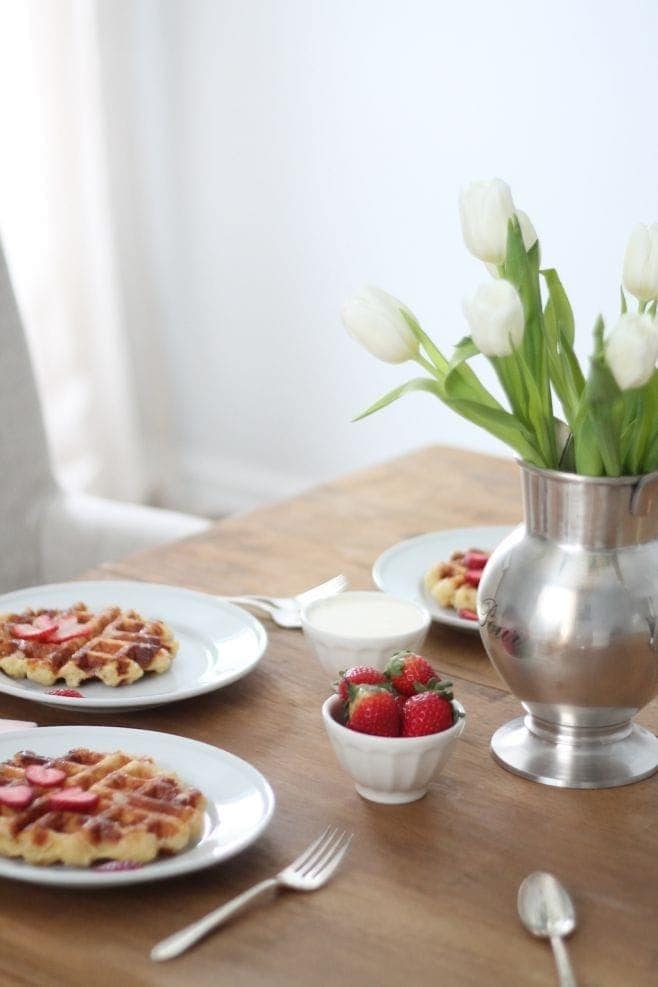 homemade belgian waffles on white plates with strawberries and plant on wooden table